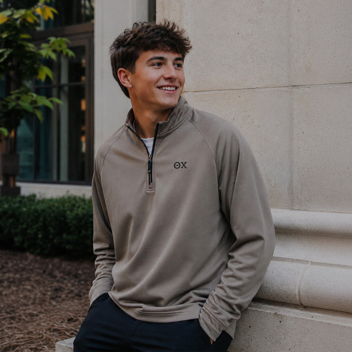 College-aged man wearing the Mushroom Cutter & Buck Adapt quarter-zip with black embroidered Theta Chi Greek letters outdoors on campus.