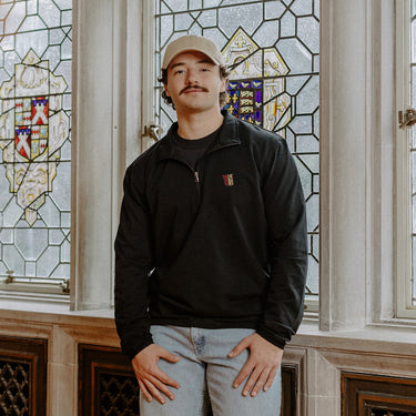 Male model wearing the black Theta Chi Embroidered Luxe Quarter Zip in front of stained glass windows with fraternity Symbols.
