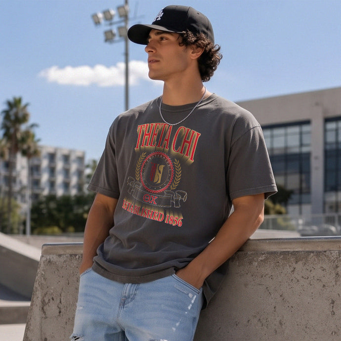 College-aged male wearing the fraternity Collegiate Crest Graphic Tee in charcoal grey, featuring vintage Theta Chi crest artwork on campus.