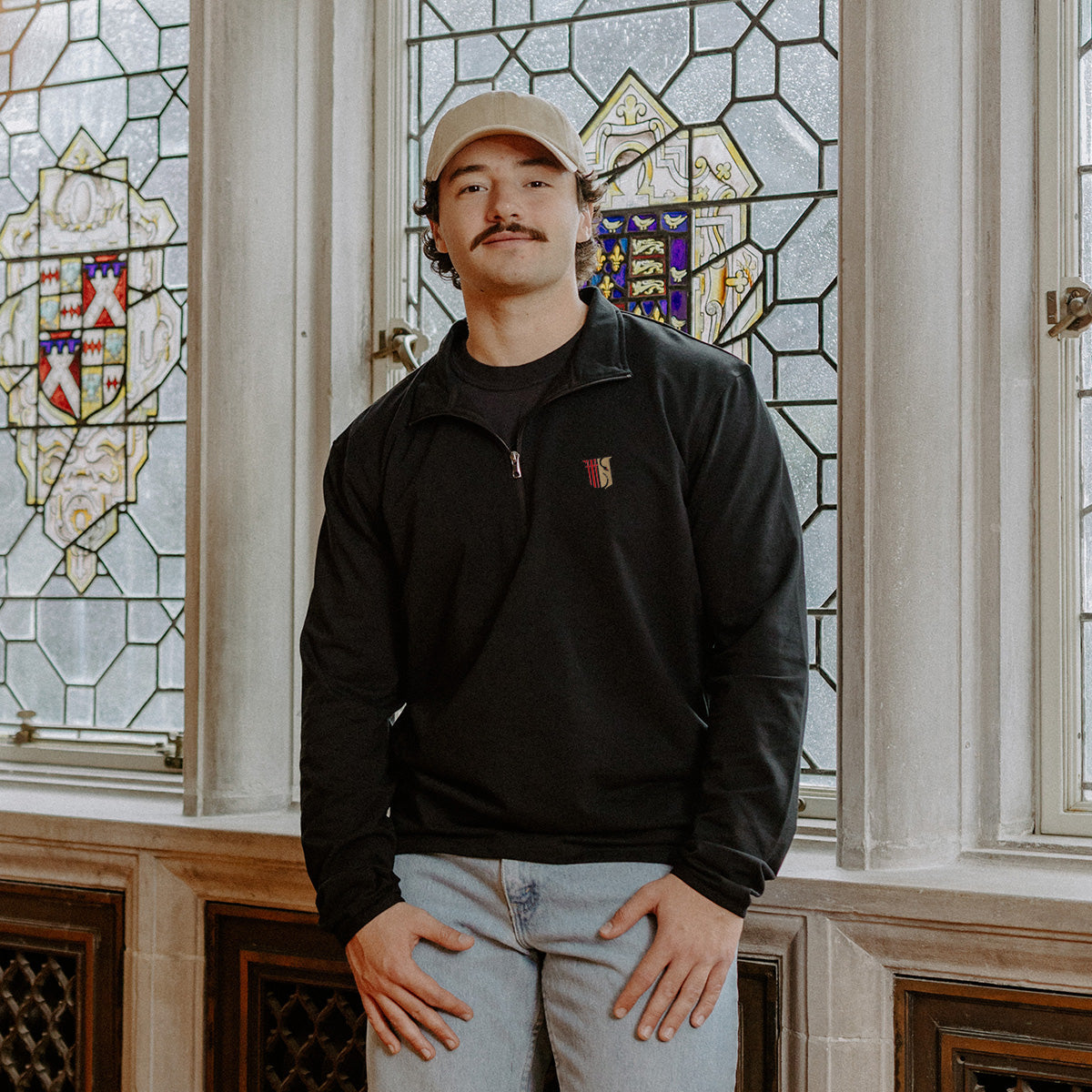 Male model wearing the black Theta Chi Embroidered Luxe Quarter Zip in front of stained glass windows with fraternity symbols.