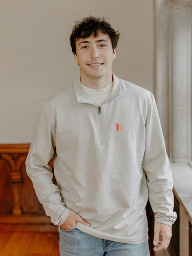 Male model wearing the smoke-colored Theta Chi Embroidered Luxe Quarter Zip with Symbol embroidery, standing by a window in a formal setting.