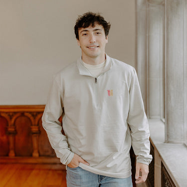 Male model wearing the smoke-colored Theta Chi Embroidered Luxe Quarter Zip with symbol embroidery, standing by a window in a formal setting.