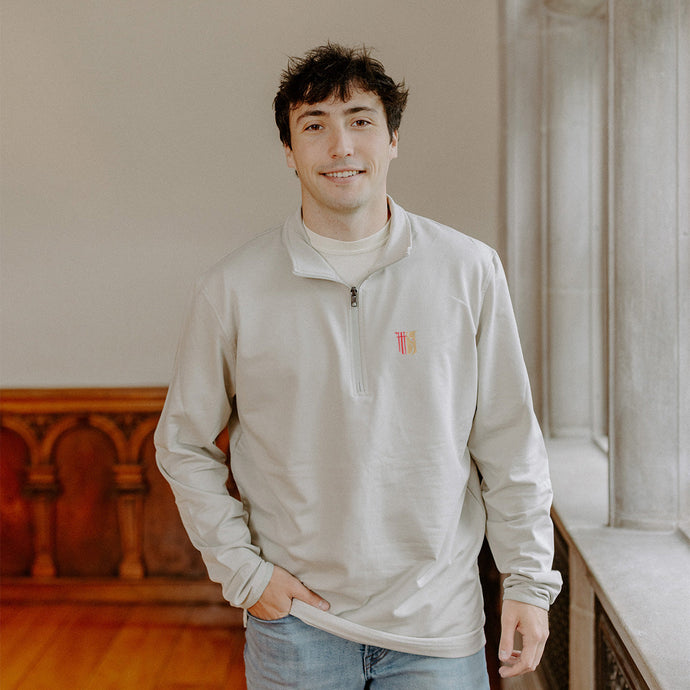 Male model wearing the smoke-colored Theta Chi Embroidered Luxe Quarter Zip with Symbol embroidery, standing by a window in a formal setting.